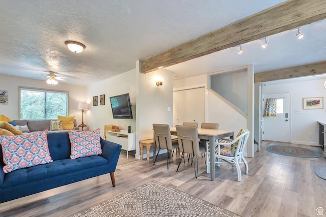 living area featuring a ceiling fan, wood finished floors, a textured ceiling, baseboards, and beamed ceiling