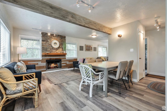 dining area with rail lighting, a fireplace, light wood-style flooring, beam ceiling, and baseboards