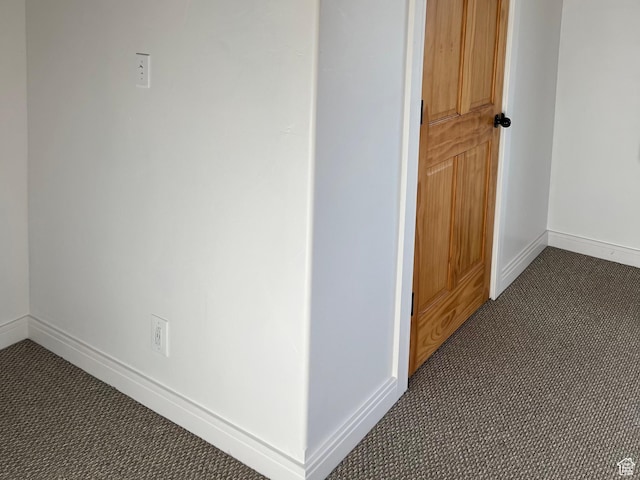 hall featuring dark carpet and baseboards