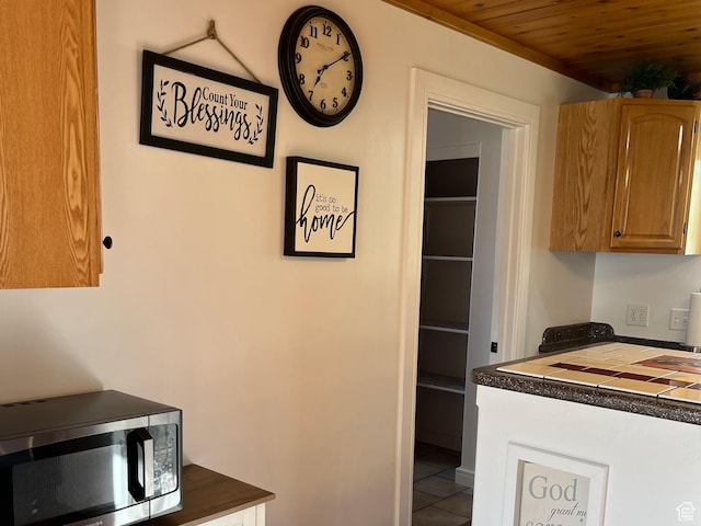 kitchen featuring stainless steel microwave, dark countertops, tile patterned flooring, wooden ceiling, and brown cabinets