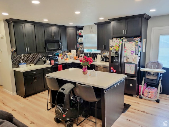 kitchen with black appliances, light wood finished floors, tasteful backsplash, light countertops, and recessed lighting