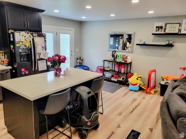 kitchen featuring black fridge with ice dispenser, light countertops, light wood-type flooring, a kitchen breakfast bar, and recessed lighting