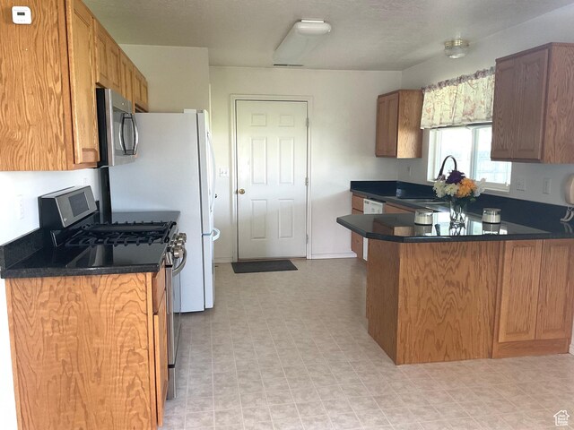 kitchen with stainless steel appliances, dark countertops, a peninsula, and a sink