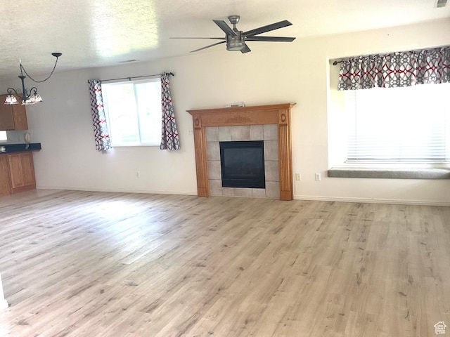 unfurnished living room with light wood-style flooring, a ceiling fan, a tile fireplace, a chandelier, and baseboards