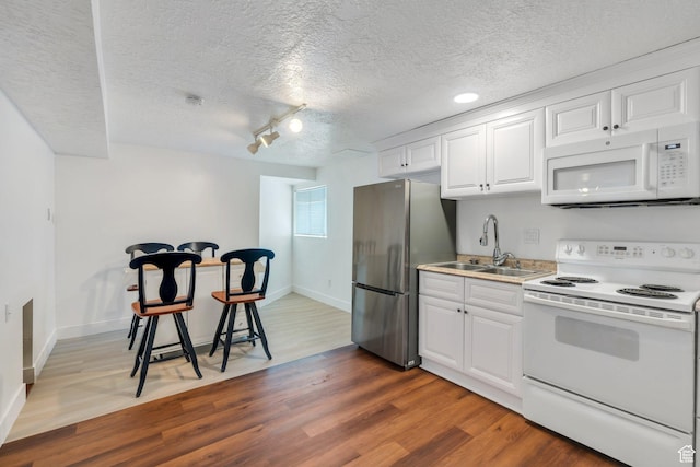 kitchen featuring white appliances, a sink, wood finished floors, white cabinets, and a textured ceiling