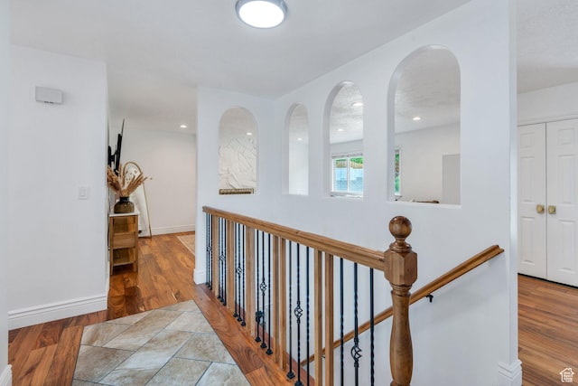 hallway featuring wood finished floors, baseboards, and an upstairs landing