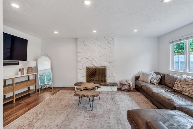 living room with wood finished floors, a textured ceiling, recessed lighting, baseboards, and a stone fireplace