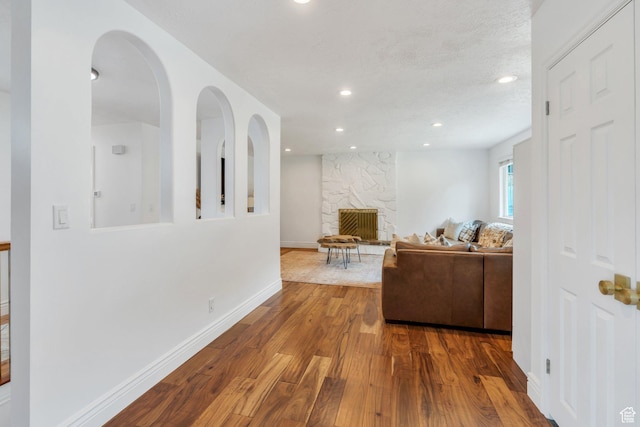 living room featuring wood finished floors, a stone fireplace, recessed lighting, and baseboards