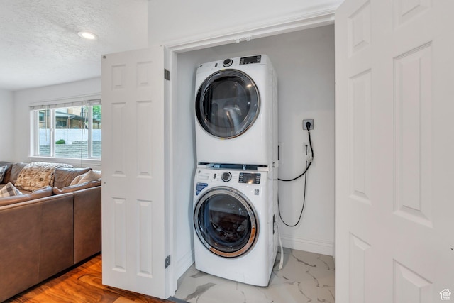 laundry area with stacked washer / drying machine, a textured ceiling, baseboards, and marble finish floors