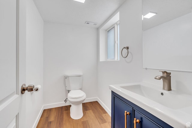 half bathroom with wood finished floors, toilet, baseboards, and vanity