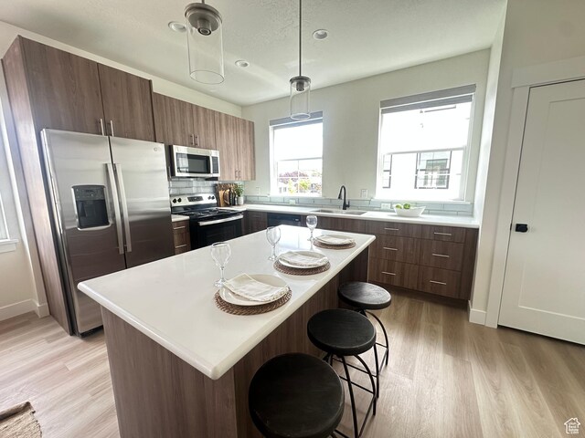 7838 S Holden St, Midvale, UT 84047 - kitchen featuring stainless steel appliances, a sink, light wood-style flooring, a breakfast bar, and light countertops