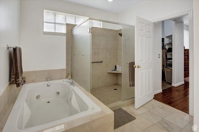 bathroom featuring a stall shower, a tub with jets, and a walk in closet