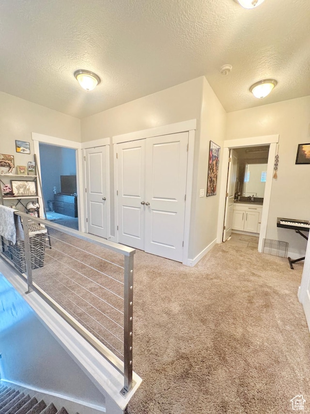 hallway featuring a textured ceiling, baseboards, and light colored carpet