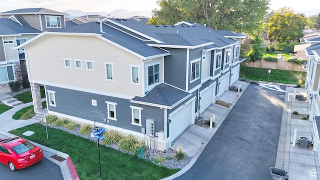 view of home's exterior featuring roof with shingles, an attached garage, a yard, and central AC