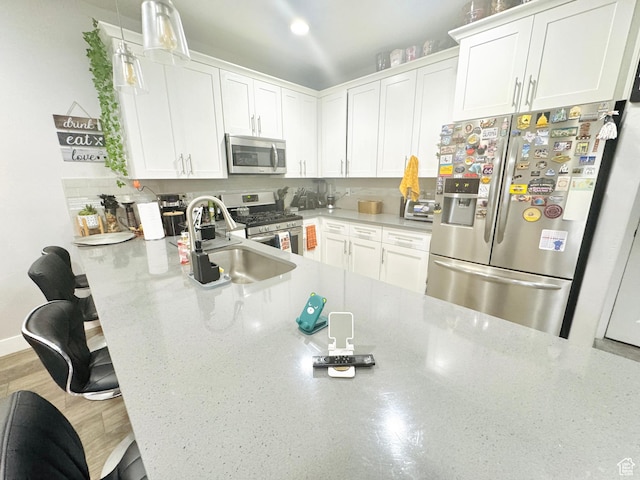 kitchen featuring stainless steel appliances, a sink, white cabinetry, a breakfast bar, and hanging light fixtures