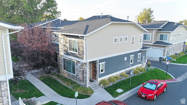 view of side of home featuring stone siding, a porch, a yard, a garage, and asphalt driveway