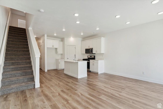 1862 S 1280 W, Logan, UT 84321 - kitchen with stainless steel appliances, a kitchen island with sink, baseboards, white cabinets, and light wood-style flooring