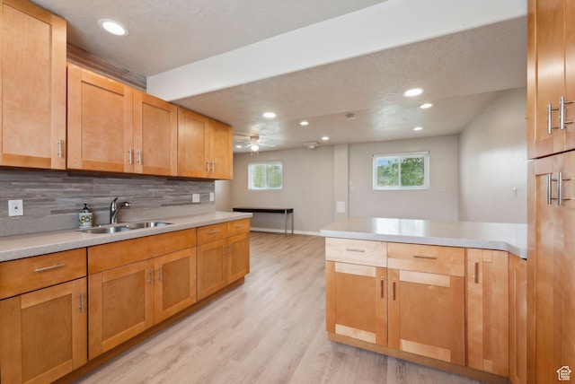 kitchen featuring a sink, a peninsula, backsplash, light wood-type flooring, and recessed lighting