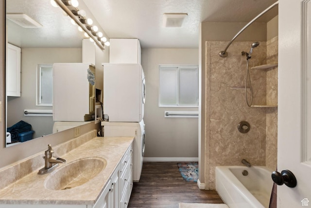 bathroom with stacked washing machine and dryer, wood finished floors, tub / shower combination, vanity, and baseboards