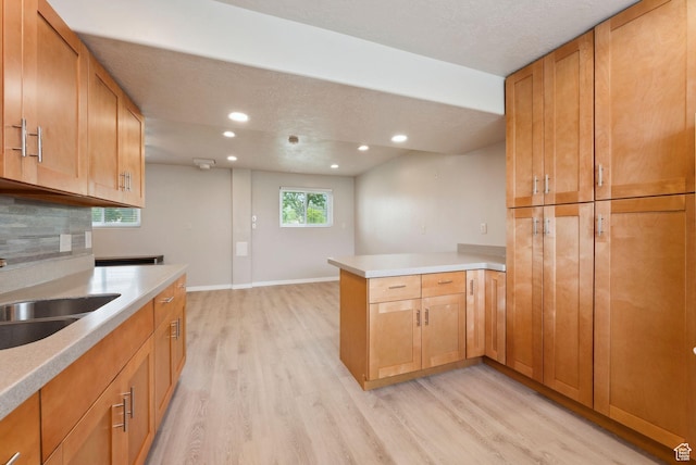 kitchen with a peninsula, light wood finished floors, a sink, recessed lighting, and light countertops