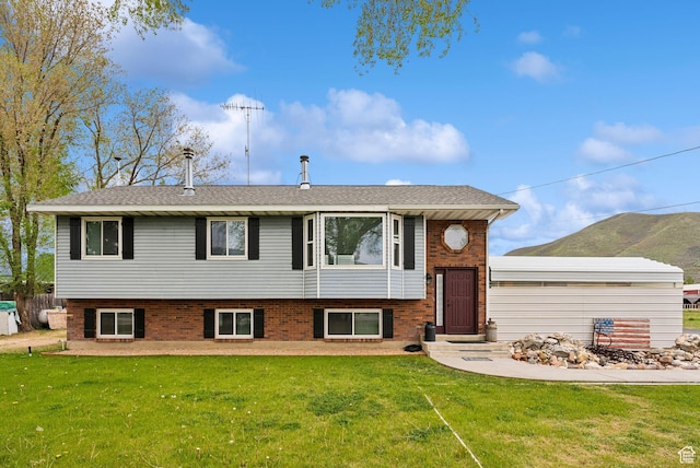 raised ranch with a front lawn, brick siding, and roof with shingles