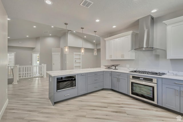 kitchen with stainless steel appliances, wall chimney exhaust hood, gray cabinetry, a peninsula, and a ceiling fan