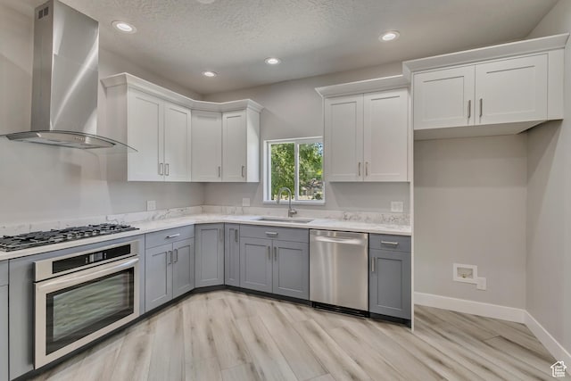 kitchen featuring appliances with stainless steel finishes, a sink, wall chimney range hood, gray cabinetry, and recessed lighting