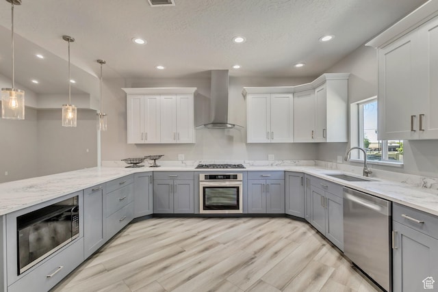 kitchen with appliances with stainless steel finishes, wall chimney range hood, a sink, gray cabinetry, and recessed lighting