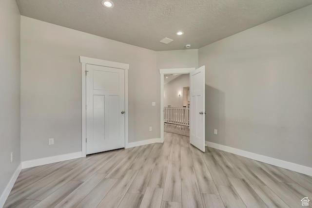 unfurnished room featuring light wood finished floors, baseboards, a textured ceiling, and recessed lighting