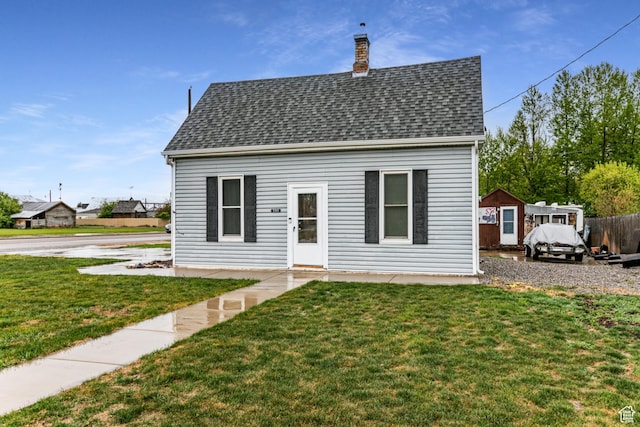 rear view of house with a shingled roof, a chimney, and a yard
