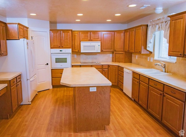 kitchen with white appliances, a sink, a center island, brown cabinetry, and recessed lighting