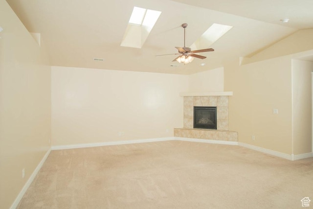 unfurnished living room featuring a skylight, light carpet, lofted ceiling, ceiling fan, and a tile fireplace