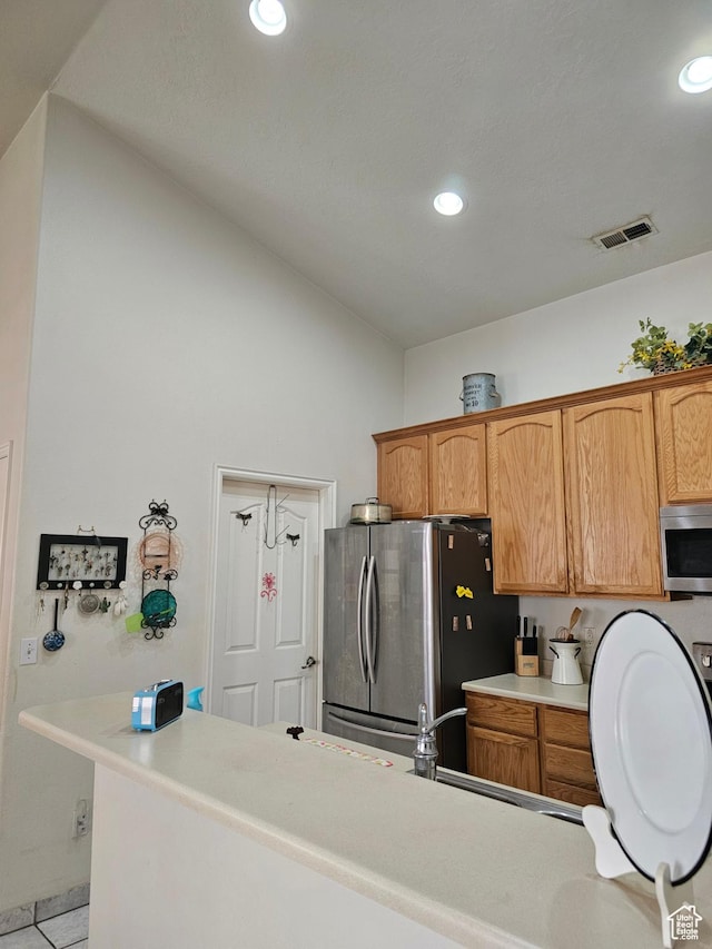 kitchen featuring appliances with stainless steel finishes, vaulted ceiling, light countertops, recessed lighting, and brown cabinetry