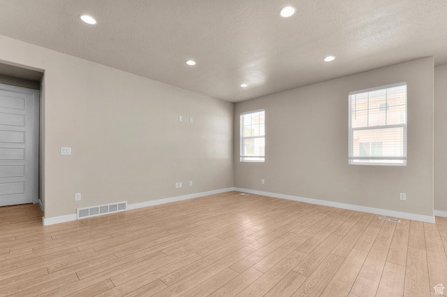 unfurnished room with light wood-style flooring, a textured ceiling, baseboards, and recessed lighting