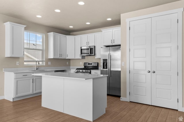 kitchen featuring appliances with stainless steel finishes, light wood-style floors, a sink, white cabinets, and recessed lighting