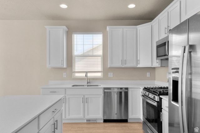 kitchen with stainless steel appliances, a sink, white cabinets, light countertops, and recessed lighting