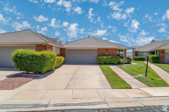 ranch-style home featuring brick siding, a tile roof, a garage, and driveway