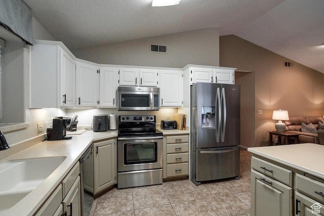 kitchen featuring stainless steel appliances, lofted ceiling, a sink, light countertops, and light tile patterned floors