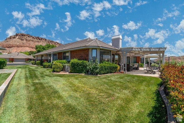 rear view of property featuring a pergola, a chimney, a lawn, a patio, and a mountain view