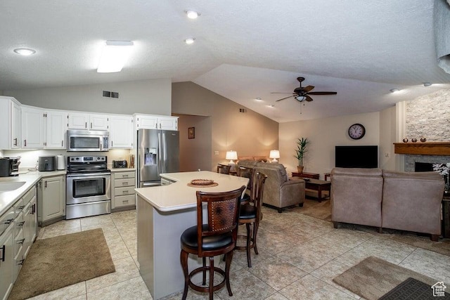 kitchen with stainless steel appliances, open floor plan, vaulted ceiling, a ceiling fan, and a breakfast bar area