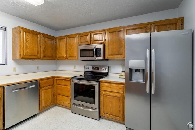 kitchen with appliances with stainless steel finishes, light countertops, brown cabinets, and a textured ceiling
