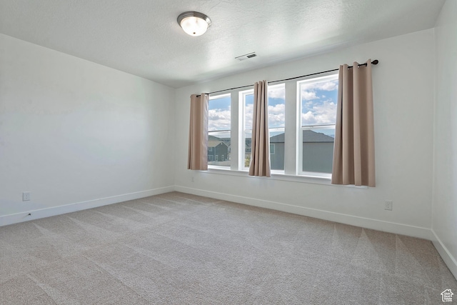 spare room featuring baseboards, a textured ceiling, and light colored carpet