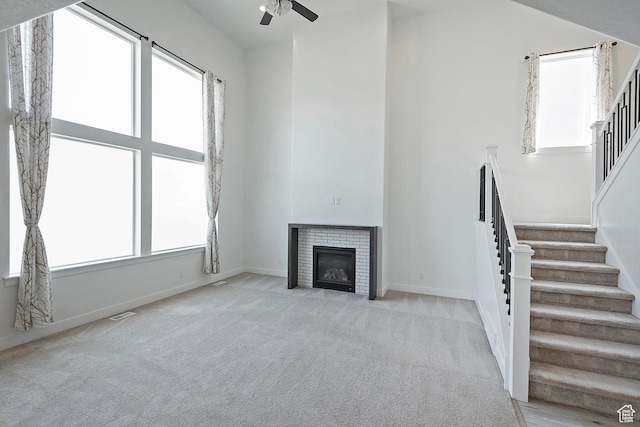 unfurnished living room featuring stairs, a ceiling fan, plenty of natural light, light colored carpet, and a high ceiling