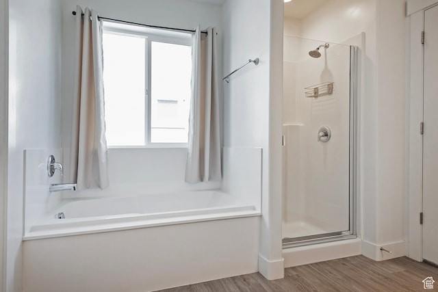 bathroom with a stall shower, plenty of natural light, wood finished floors, and a tub to relax in