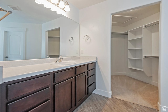 bathroom with wood finished floors, a spacious closet, baseboards, and vanity