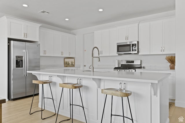 1445 N Arena Roja Dr, Washington, UT 84780 - kitchen featuring stainless steel appliances, white cabinetry, light wood-type flooring, an island with sink, and a sink