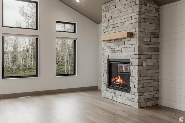 unfurnished living room with a stone fireplace, wood finished floors, high vaulted ceiling, and baseboards