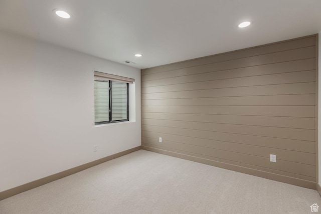 spare room with baseboards, light colored carpet, recessed lighting, and wooden walls