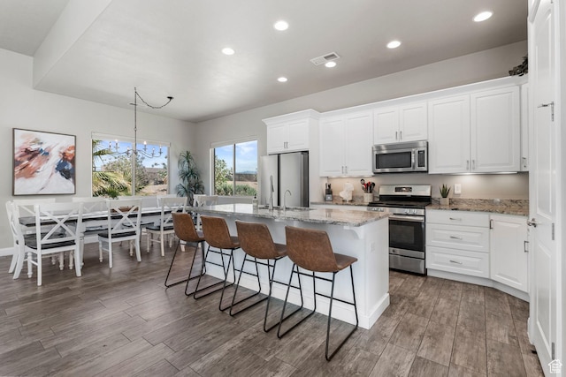 3258 S 4900 W, Hurricane, UT 84737 - kitchen with appliances with stainless steel finishes, a kitchen island with sink, wood finished floors, white cabinets, and a breakfast bar