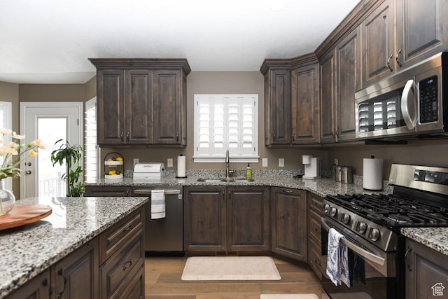 kitchen featuring appliances with stainless steel finishes, a sink, light wood-style flooring, and dark brown cabinets